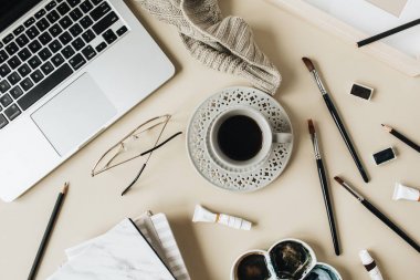 Suluboya sanatçı ev ofis masası çalışma alanı bej arka plan üzerinde. Dizüstü bilgisayar, kahve fincanı, boya fırçaları, ekose, boyama, suluboya. Düz lay, üst görünüm blog, sosyal medya, web sitesi şablonu.