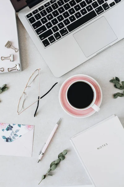 Minimal home office desk workspace with laptop, coffee, notebook, eucalyptus, envelope. Flat lay, top view social media background.