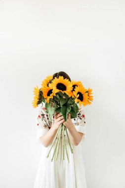 Beyaz elbise genç güzel kadın beyaz arka planda ayçiçeği buket tutun. Floral minimal kompozisyon.