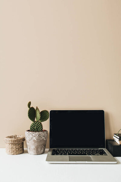 Minimalist home office desk workspace with laptop, cactus on beige background. Front view copy space blank mock up. 