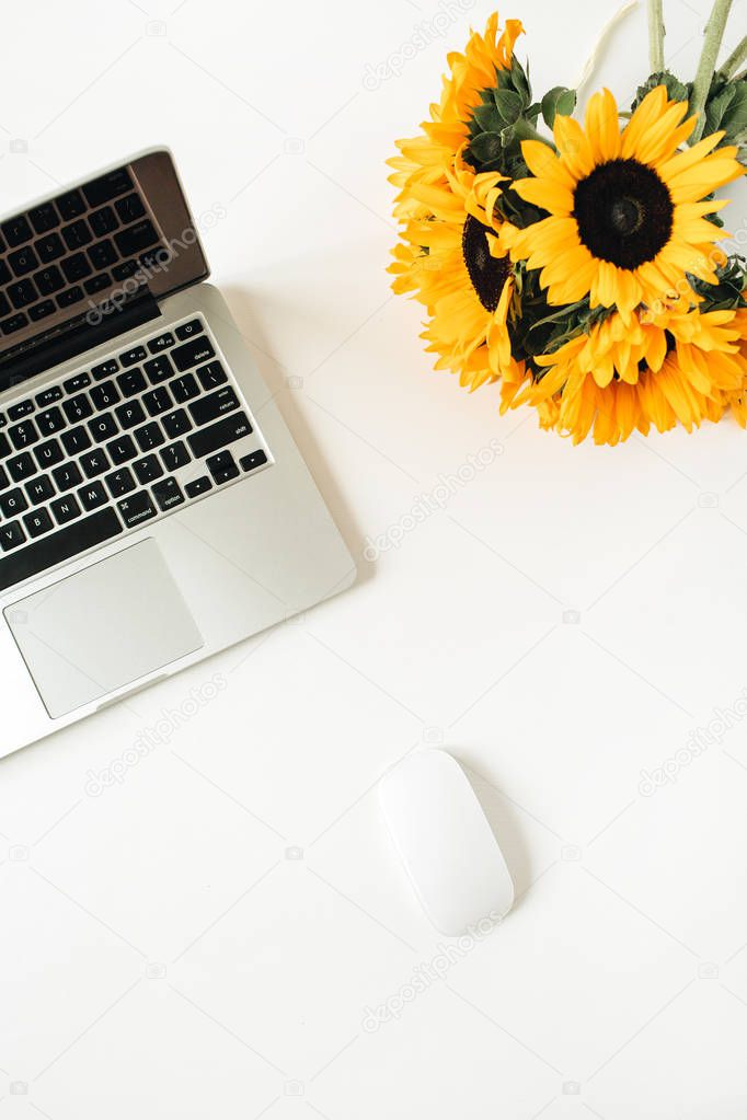 Home office desk workspace with laptop, yellow sunflowers bouquet on white background. Flat lay, top view freelancer / blogger work concept.