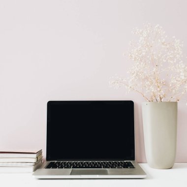 Dizüstü bilgisayar ile minimalist ev ofis masası çalışma alanı, pembe arka plan üzerinde çiçek buketi. Boş kopyalama alanı olan ön görünüm kahraman üstbilgisi.