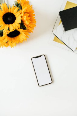 Akıllı telefon mockup, Notebook, beyaz arka planda sarı ayçiçeği buket ile ev ofis masası çalışma. Düz yatıyordu, üst görünüm Freelancer/Blogger çalışma kavramı.