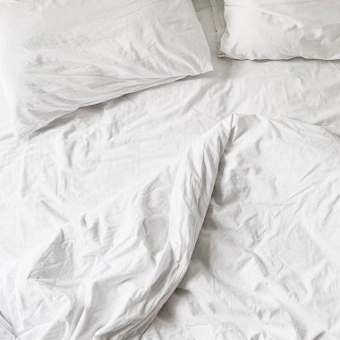Düz yatıyordu, çarşaf, battaniye ve iki yastık ile beyaz keten üst görünümü. Minimal yatak konsepti.