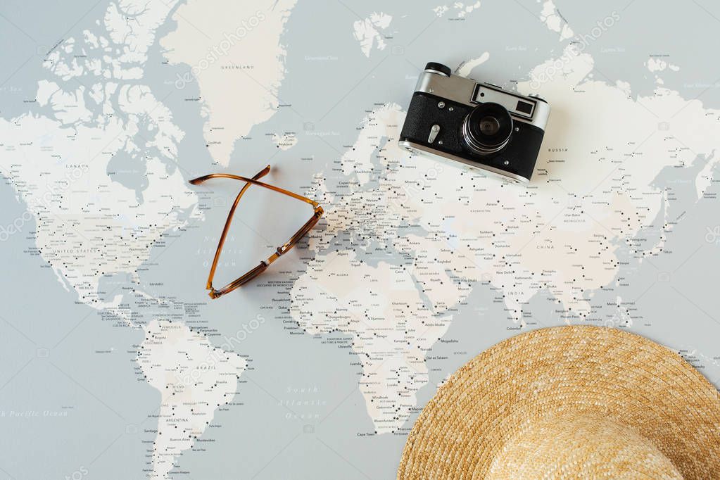 Minimal world map with pins, retro camera, sunglasses, straw hat. Flat lay vacation travel planning composition. Travel photographer concept.