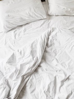 Düz yatıyordu, çarşaf, battaniye ve iki yastık ile beyaz keten üst görünümü. Minimal yatak konsepti.