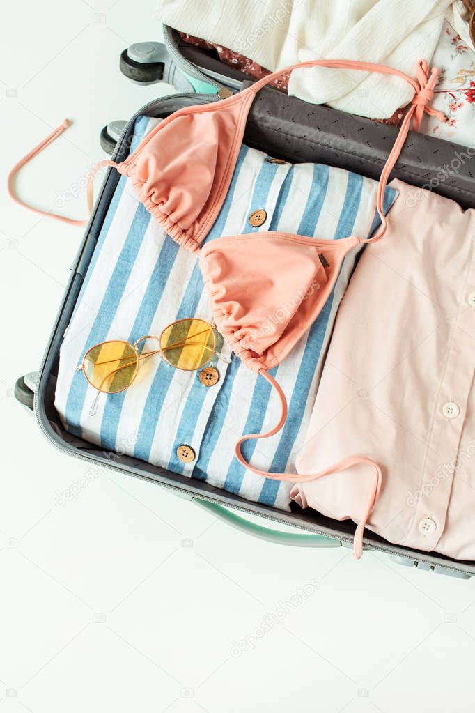 Hand luggage with bikini, sunglasses and dress. Flat lay, top view travel vacation fashion composition.
