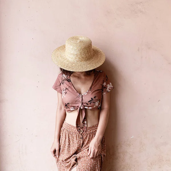 Moda kadın kavramı. Pembe etekli genç kadın, kısa pembe bluz ve saman şapka pembe duvarın yanında duruyor. Güzellik günlüğü.