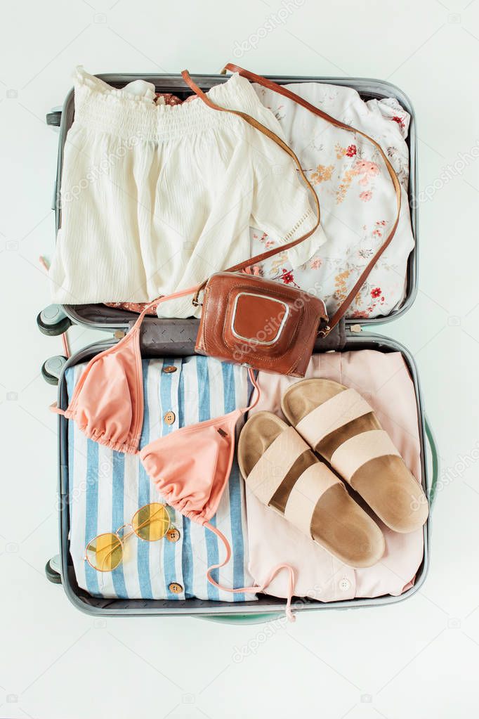 Women's summer bikini swimsuit, stylish sunglasses retro camera, slippers and dress in luggage. Flat lay, top view fashion travel lifestyle concept.