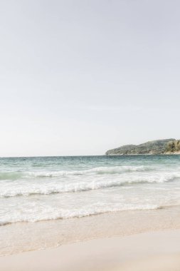 Phuket, Tayland ufukta dalgalar ve yeşil ada ile beyaz kum, mavi deniz ile güzel tropikal plaj manzarası. Nötr renklerle minimal kompozisyon. Yaz konsepti. Doğal arka plan.