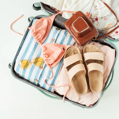 Mayo bikini, terlik, güneş gözlüğü, elbise, beyaz arka planda retro kamera ile seyahat el bagajı. Düz lay, üst görünüm yaz tatili konsepti.