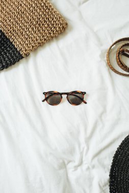 Fotoğraf ve kemer, hasır şapka, beyaz çarşaf ile yatakta yatan saman çanta ortasında gözlük ile kadın moda aksesuarları. Yaz ve seyahat konsepti. Üst görünüm, düz yatıyordu. 