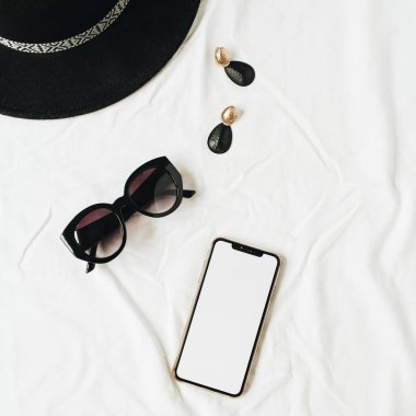 Beyaz keten zarif kadın aksesuarları ile moda mockup kompozisyon. Şapka, güneş gözlüğü, küpe, fotokopi uzay ekranı ile akıllı telefon. Düz yatıyordu, üst görünümü minimal yaşam tarzı moda blog konsepti.