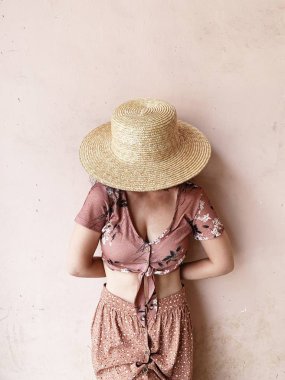Moda kadın kavramı. Pembe etekli genç kadın, kısa pembe bluz ve saman şapka pembe duvarın yanında duruyor. Güzellik günlüğü.