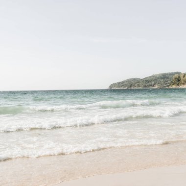 Phuket, Tayland ufukta dalgalar ve yeşil ada ile beyaz kum, mavi deniz ile güzel tropikal plaj manzarası. Nötr renklerle minimal kompozisyon. Yaz konsepti. Doğal arka plan.