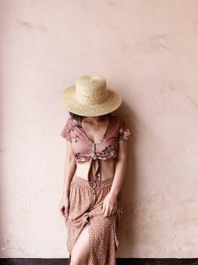 Moda kadın kavramı. Pembe etekli genç kadın, kısa pembe bluz ve saman şapka pembe duvarın yanında duruyor. Güzellik günlüğü.