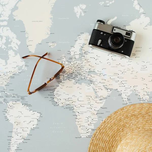 Minimal world map with pins, retro camera, sunglasses, straw hat. Flat lay vacation travel planning composition. Travel photographer concept.