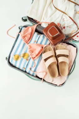 Mayo bikini, terlik, güneş gözlüğü, elbise, beyaz arka planda retro kamera ile seyahat el bagajı. Düz lay, üst görünüm yaz tatili konsepti.