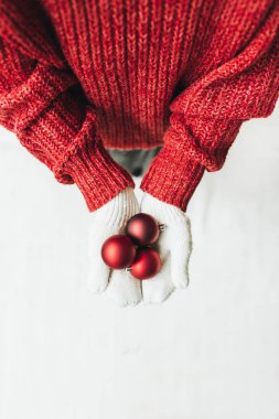 Noel / Yeni Yıl / Noel kompozisyonu. Kırmızı örgü süveter ve kırmızı Noel oyuncakları tutan beyaz eldivenli genç bir kadın. Düz yerde, üst tarafta. En az kış tatili konsepti.