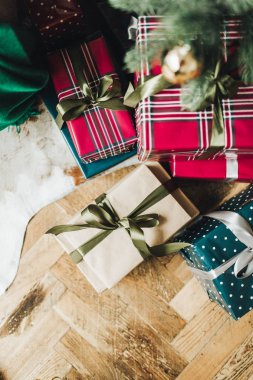 Noel / Yeni Yıl kompozisyonu. Noel ağacı altında ahşap zeminde duran kırmızı, mavi ve bej renkli kağıtlarla süslenmiş el yapımı hediye kutuları. Düz yerde, üst tarafta. Kış tatili kavramı.