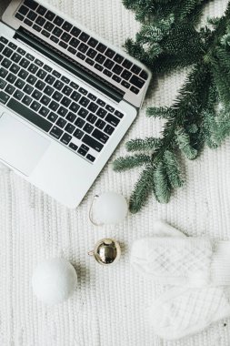 Noel / Yeni Yıl / Noel kompozisyonu. Düz yerde, üst tarafta. Laptop, Noel ağacı dallarıyla süslenmiş beyaz battaniyenin üzerinde duruyor. Beyaz ve altın renkli şenlikli toplar, beyaz eldivenler. Asgari iş serbest konsepti.