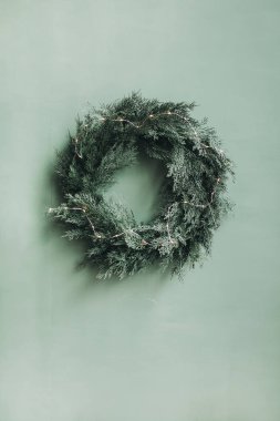 Noel / Yeni Yıl kompozisyonu. Noel ağacından yapılmış şenlikli çelenk, soluk yeşil duvarda köknar dalları ve çelenkler. En az kış tatili konsepti.
