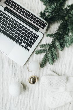 Noel / Yeni Yıl / Noel kompozisyonu. Düz yerde, üst tarafta. Laptop, Noel ağacı dallarıyla süslenmiş beyaz battaniyenin üzerinde duruyor. Beyaz ve altın renkli şenlikli toplar, beyaz eldivenler. Asgari iş serbest konsepti.