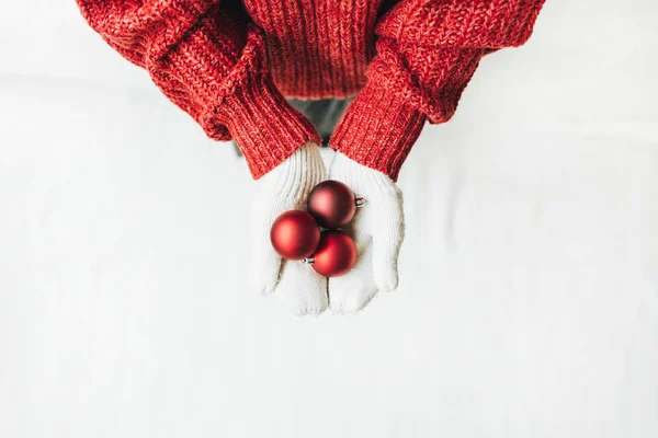 クリスマス クリスマスの構成 赤いニットのセーターと白いミトンの若い女性が木の赤いクリスマスのおもちゃを持っています フラットレイアウト トップビュー 最低冬休みのコンセプト — ストック写真