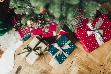 Noel / Yeni Yıl kompozisyonu. Noel ağacı altında ahşap zeminde duran kırmızı, mavi ve bej renkli kağıtlarla süslenmiş el yapımı hediye kutuları. Düz yerde, üst tarafta. Kış tatili kavramı.