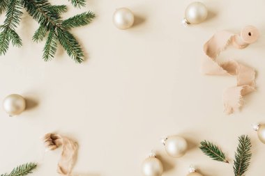 Noel / Yeni Yıl bayramı kompozisyonu. Çerçeveyi, köknar iğnesi dallarından, kurdelelerden ve bej arkaplandaki Noel mücevherlerinden oluşan boş bir kopya alanı ile düzenle. Düz konum, üst manzara şenlik konsepti.