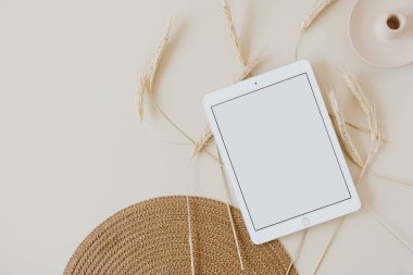 Bej arka planda, buğday sapı ve hasır peçeteli tablet. Düz konum, üst görünüm kopyalama alanı şablonu. Evde asgari iş, yaşam tarzı konsepti.