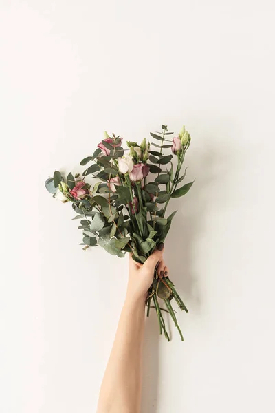 Women's hand holding roses flowers bouquet against white wall. Holiday celebration, wedding background