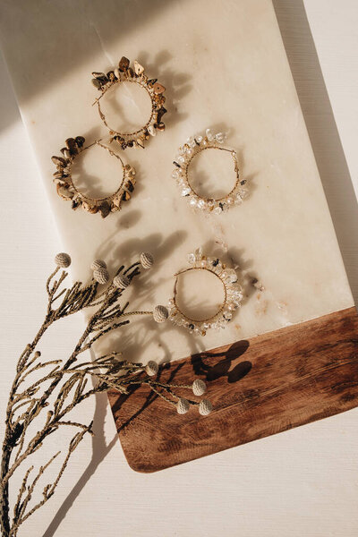 Trendy handmade earrings and floral branch on marble board on white background. Flat lay, top view minimal fashion bijouterie concept with sunlight shadows.