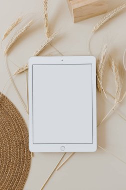Bej arka planda, buğday sapı ve hasır peçeteli tablet. Düz konum, üst görünüm kopyalama alanı şablonu. Evde asgari iş, yaşam tarzı konsepti.