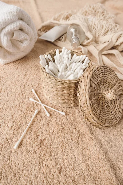 Beauty spa composition with ear sticks in rattan casket, towel, string bag on beige towel. Female beauty treatment routine concept.