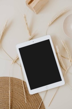 Bej arka planda, buğday sapı ve hasır peçeteli tablet. Düz konum, üst görünüm kopyalama alanı şablonu. Evde asgari iş, yaşam tarzı konsepti.