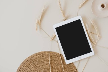 Bej arka planda, buğday sapı ve hasır peçeteli tablet. Düz konum, üst görünüm kopyalama alanı şablonu. Evde asgari iş, yaşam tarzı konsepti.
