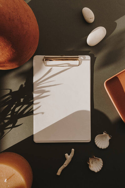 Чистый лист бумаги планшет с макетом копировального пространства, камни, ракушки, кораллы, свечи, глиняный горшок в цветочных солнечных тенях на глубоком зеленом фоне. Квартира лежала, вид сверху был пуст