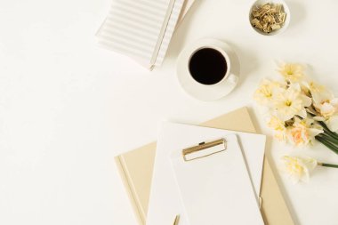 Merkez ofis masa çalışma alanı. Fotokopi alanı, kahve fincanı, narsisli çiçekler, beyaz arka planda kırtasiye malzemesi olan boş bir not defteri. Düz yerde, üst tarafta. Evde çalışmak, iş, serbest meslek kavramı