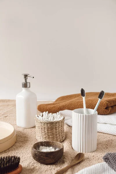 Beauty health care composition with ear sticks in rattan casket, towel, liquid soap, toothbrushes on beige towel. Female beauty treatment routine concept