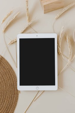 Bej arka planda, buğday sapı ve hasır peçeteli tablet. Düz konum, üst görünüm kopyalama alanı şablonu. Evde asgari iş, yaşam tarzı konsepti.