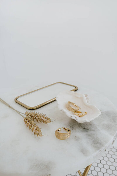 Минимальная модная композиция с золотыми серьгами в раковине на мраморном столе с зеркальными и пшеничными стеблями. Бижутерия / ювелирная концепция
.