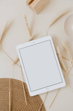 Bej arka planda, buğday sapı ve hasır peçeteli tablet. Düz konum, üst görünüm kopyalama alanı şablonu. Evde asgari iş, yaşam tarzı konsepti.