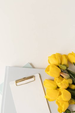 Merkez ofis masa çalışma alanı. Taklit yeri olan boş bir pano defteri, beyaz arka planda lale çiçekleri. Düz yerde, üst tarafta. Evde çalışmak, dış kaynak kullanımı, serbest çalışma kavramı.