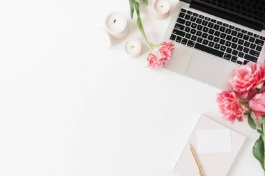 Laptop ve güzel pembe şakayık lale çiçekleri, boş kağıt kağıtlar, beyaz arka planda mumlar. Düz konum, üst görünüm minimalist ofis ofis çalışma alanı boş kopya alanı
