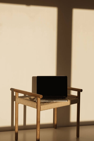 Laptop on wicker bench in sunlight shadows on the wall