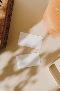 Sahte kopya alanı olan boş kağıt kağıtlar, tahta tabut ve bej arka planda güneş ışığı gölgesi olan mum. Düz konum, üst görünüm minimal ticari marka şablonu