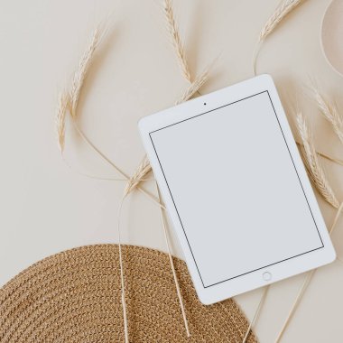 Bej arka planda, buğday sapı ve hasır peçeteli tablet. Düz konum, üst görünüm kopyalama alanı şablonu. Evde asgari iş, yaşam tarzı konsepti.