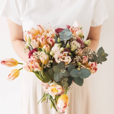 Beyaz bluzlu genç ve güzel bir kadın lale çiçeği buketini elinde beyaz duvara karşı tutuyor. Bayram kutlaması çiçek konsepti