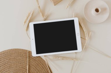 Bej arka planda, buğday sapı ve hasır peçeteli tablet. Düz konum, üst görünüm kopyalama alanı şablonu. Evde asgari iş, yaşam tarzı konsepti.
